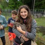 Camper smiling while holding a small animal at Long Lake Camp Adventures farm area.