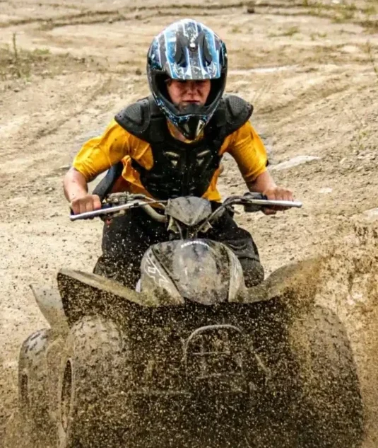 Child riding an ATV through mud during off-road camp activity
