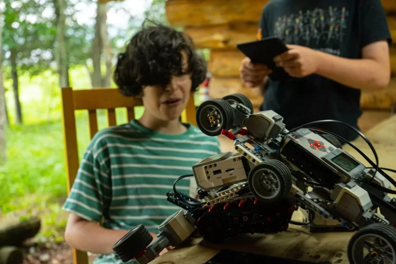 Camper working on a custom-built robotics vehicle while another camper uses a tablet to control or program it during a tech activity at camp.