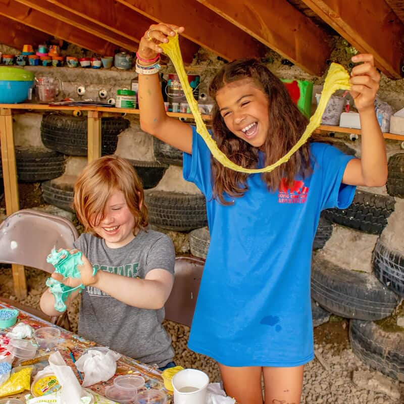 Two campers enjoying a fun crafting activity as they stretch and play with colorful slime inside the camp workshop.