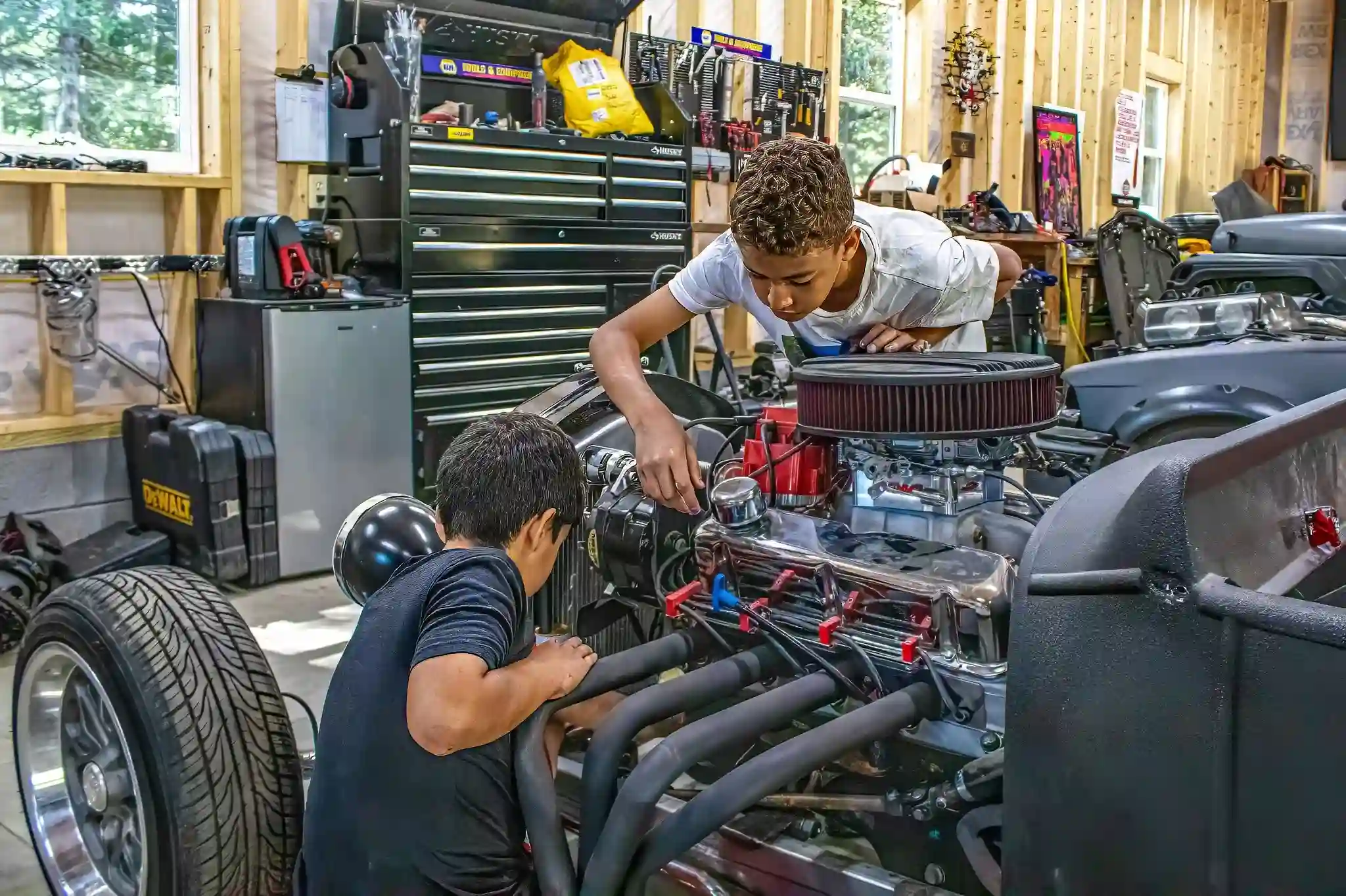 Two campers working on restoring a classic muscle car engine in a garage.