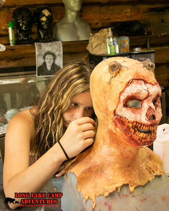 Camper covered in colorful fake blood and special effects makeup demonstrating practical horror makeup techniques at night.