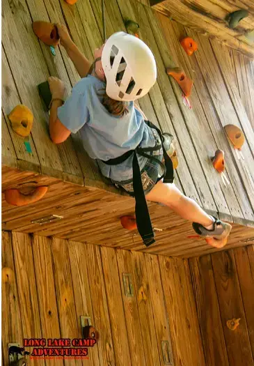 Young camper climbing the wooden rock wall at Long Lake Camp Adventures.