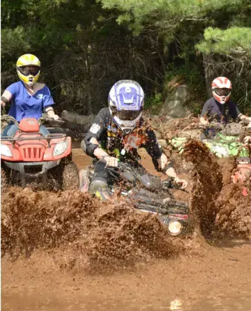 Campers riding ATVs through a muddy trail at Long Lake Camp Adventures adventure camp.