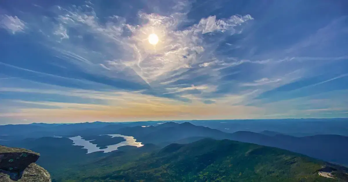 Panoramic view of Adirondack mountains and lakes under a bright summer sky.