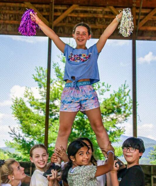 Group of campers smiling and performing cheerleading stunts at Long Lake Camp Adventures