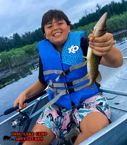 Young camper smiling and holding his catch at Long Lake Camp Adventures fishing camp.